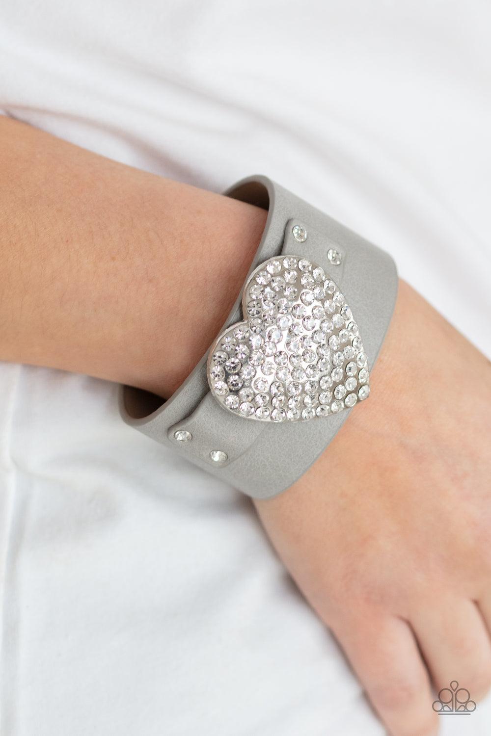 Paparazzi Accessories Flauntable Flirt - Silver Encrusted in blinding white rhinestones, an oversized silver heart frame is studded in place across the front of a gray leather band, creating a flirtatious centerpiece around the wrist. Features an adjustab