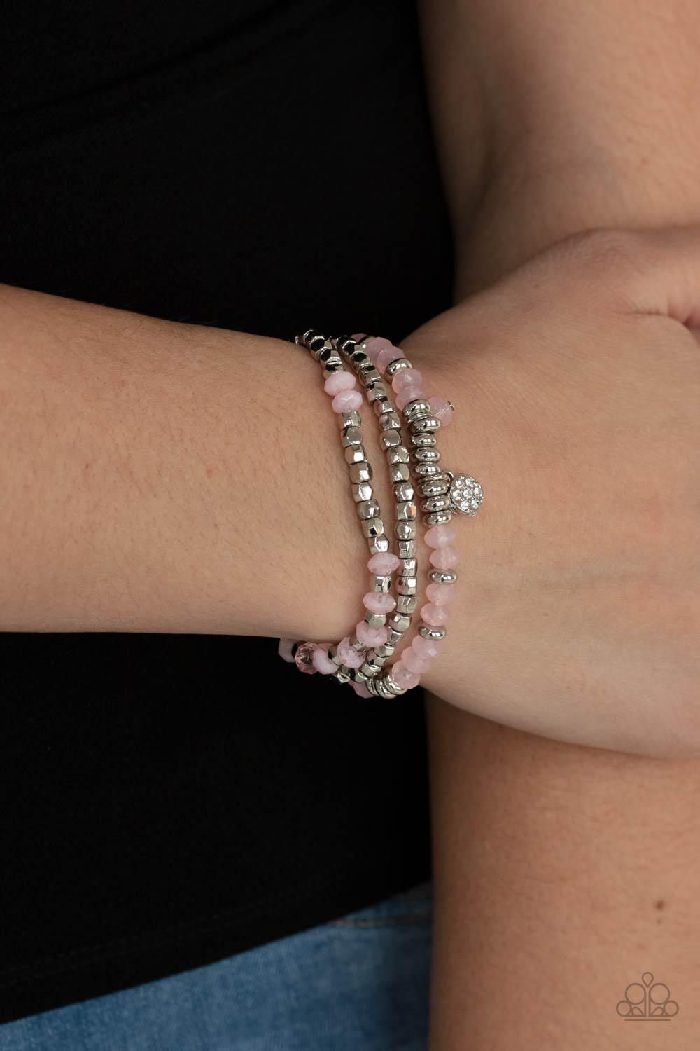 Paparazzi Accessories Glacial Glimmer - Pink A glimmering collection of silver discs, silver cube beads, and opaque pink crystal-like beads are threaded along stretchy bands around the wrist, creating icy layers. A matching opaque crystal and white rhines