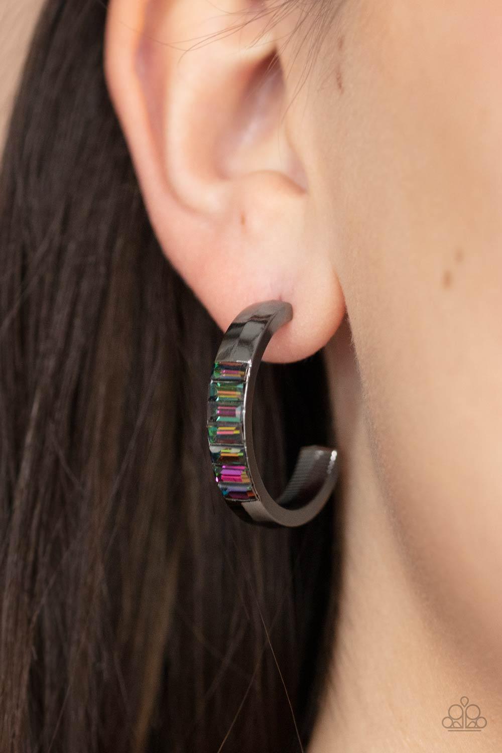 Paparazzi Accessories Bursting With Brilliance - Multi The front of a thick gunmetal hoop is encrusted in oil spill emerald cut rhinestones, creating a glamorous pop of color. Earring attaches to a standard post fitting. Hoop measures approximately 1" in