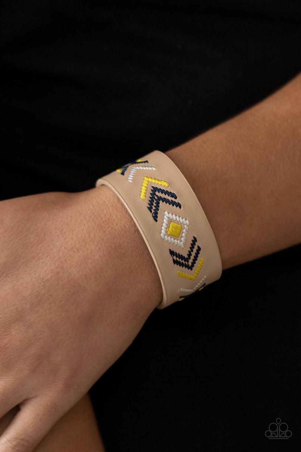 Paparazzi Accessories Cliff Glyphs - Yellow Yellow, blue, and white thread is stitched across the front of a brown leather band, creating a colorful tribal inspired pattern. Features an adjustable snap closure. Sold as one individual bracelet. Jewelry