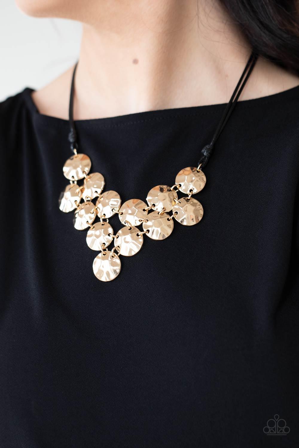 Paparazzi Accessories Token Treasure - Gold Featuring a hammered finish, a collection of glistening gold discs delicately connect into a netted pendant at the bottom of knotted black cords for a statement-making look. Features an adjustable clasp closure.