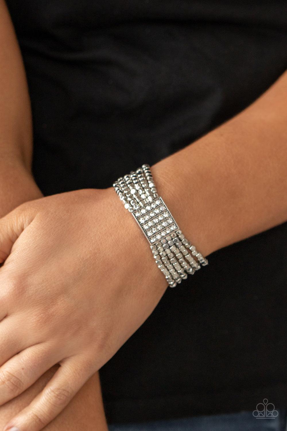 Paparazzi Accessories Star-Studded Showcase - White Held in place by a square centerpiece encrusted in row after row of dazzling rhinestones, a dainty collection of silver cube beads are threaded along stretchy bands around the wrist, creating shimmery la