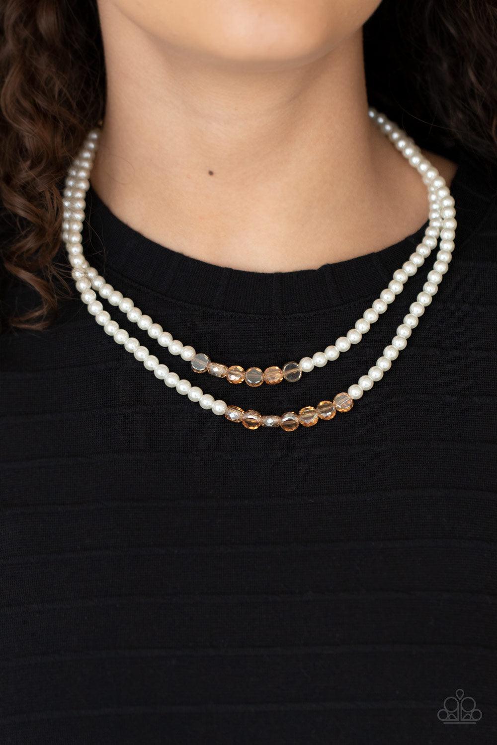 Paparazzi Accessories Poshly Petite - Gold A posh collection of pearly white beads, accented with sections of flat, faceted shimmery transparent gold beads, is threaded along invisible wires, creating sophisticated layers that fall below the collar. Featu