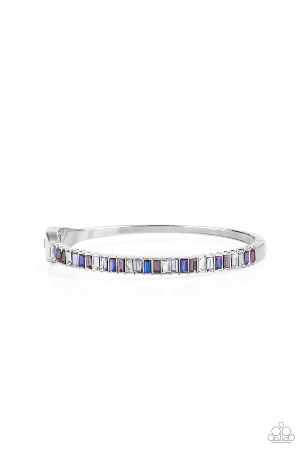Paparazzi Accessories Toast to Twinkle - Purple Featuring regal emerald style cuts, a dainty row of purple, white, and blue rhinestones are encrusted across the front of a silver cuff-like bangle for a timeless fashion. Features a hinged closure. Sold as
