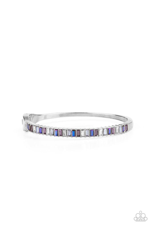 Paparazzi Accessories Toast to Twinkle - Purple Featuring regal emerald style cuts, a dainty row of purple, white, and blue rhinestones are encrusted across the front of a silver cuff-like bangle for a timeless fashion. Features a hinged closure. Sold as