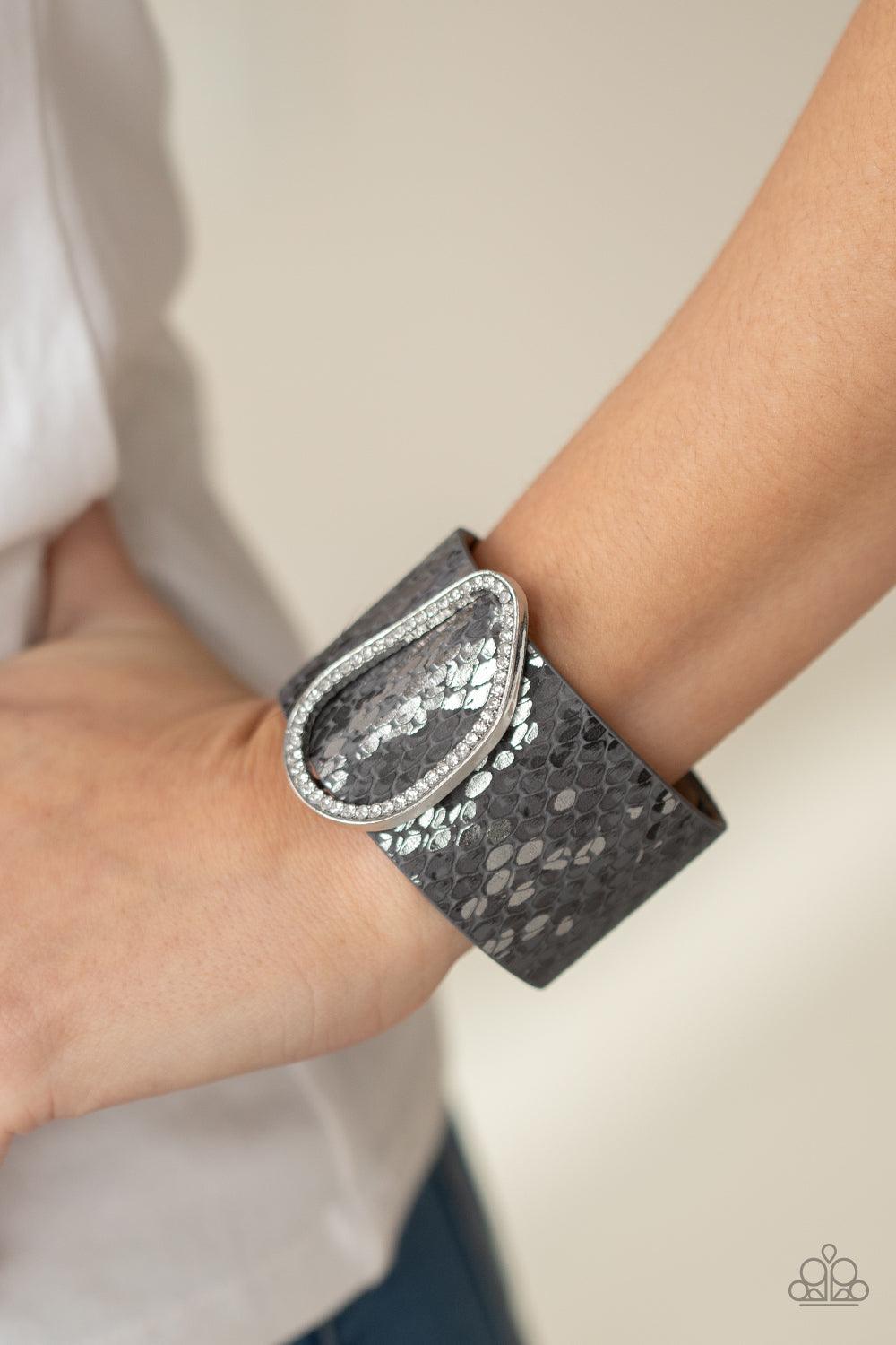 Paparazzi Accessories HISS-tory In The Making - Silver Encrusted with glassy white rhinestones, an asymmetrical silver fitting glides along a gray leather band adorned in a metallic python print for a wild look. Features an adjustable snap closure. Sold a