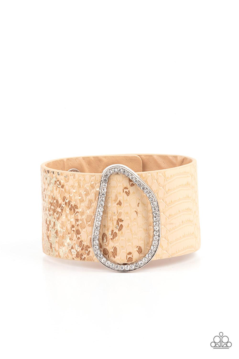 Paparazzi Accessories HISS-tory In The Making - Brown Encrusted with glassy white rhinestones, an asymmetrical silver fitting glides along a tan leather band adorned in a golden metallic python print for a wild look. Features an adjustable snap closure. S