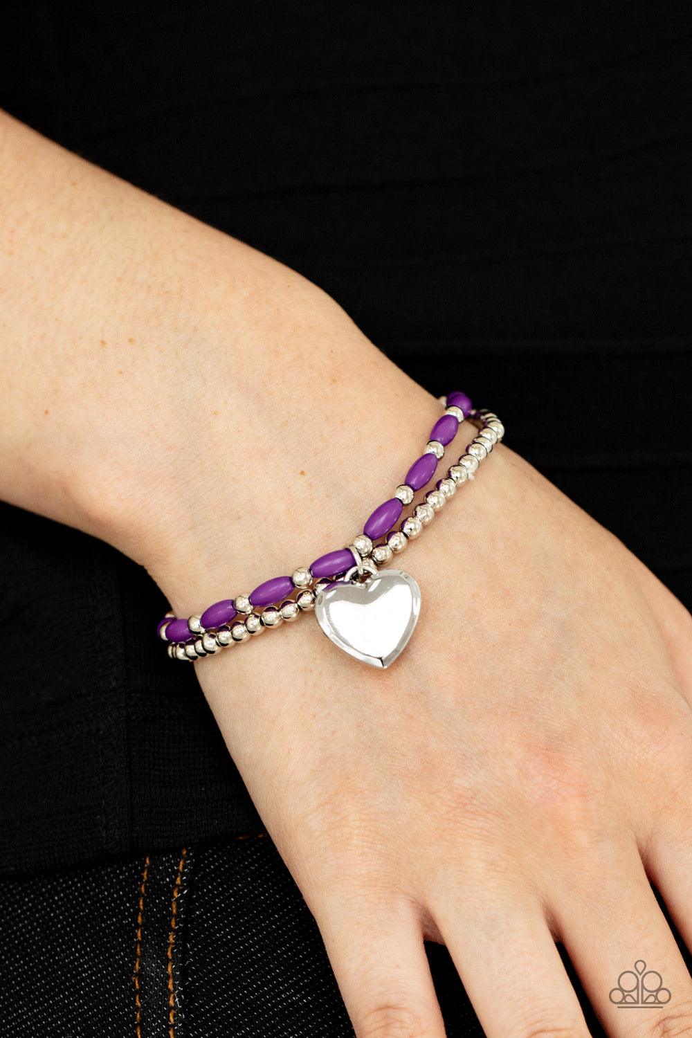 Paparazzi Accessories Candy Gram - Purple A shiny silver heart dangles from a strand of playful purple beads. It is paired with a strand of round silver beads threaded along a stretchy band for a whimsical charm around the wrist. Sold as one pair of brace