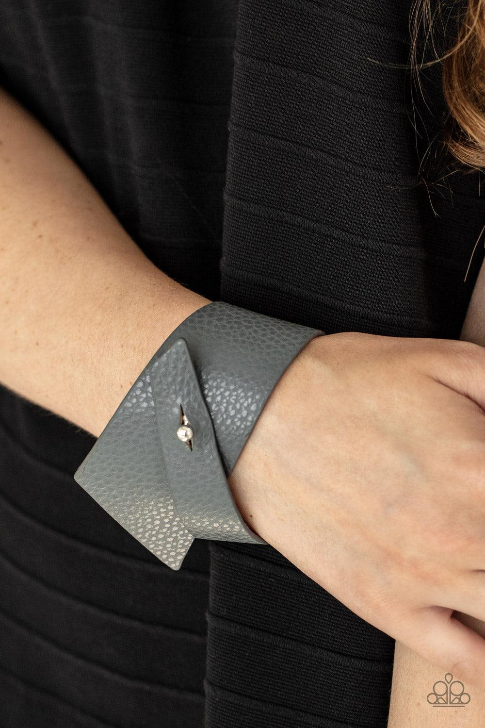 Paparazzi Accessories PIECE Offering - Silver A triangular piece of Ultimate Gray leather delicately wraps around the wrist, creating an edgy asymmetrical centerpiece around the wrist. Features a studded button loop closure. Sold as one individual bracele