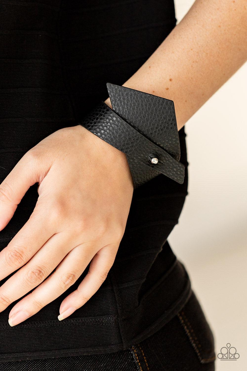 Paparazzi Accessories PIECE Offering - Black A triangular piece of black leather delicately wraps around the wrist, creating an edgy asymmetrical centerpiece around the wrist. Features a studded button loop closure. Sold as one individual bracelet. Bracel