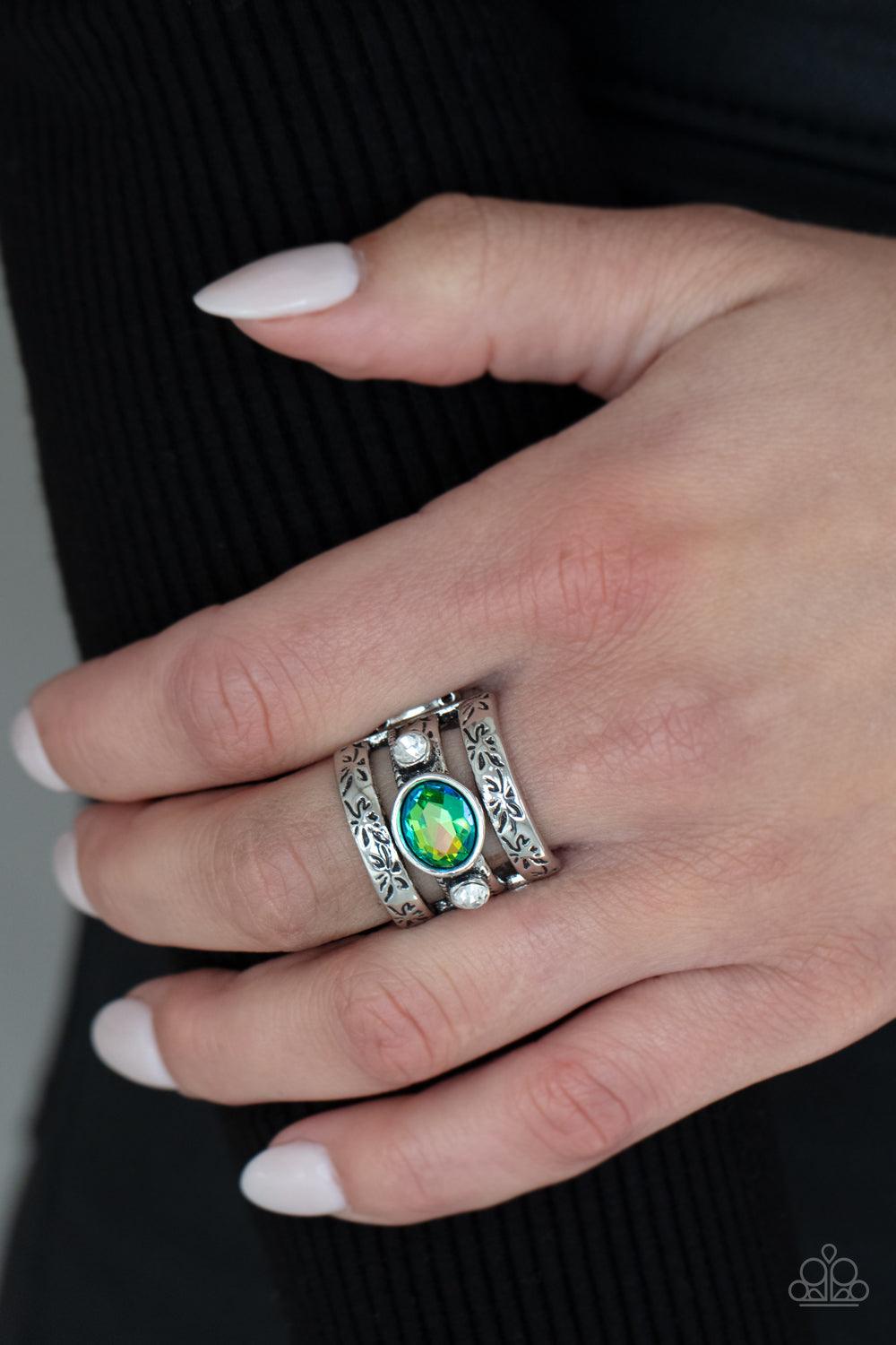 Paparazzi Accessories The GLEAMING Tower - Green A gleaming iridescent green oval cut gem sits atop a silver metal bar with smaller white rhinestones resting on either side. Silver bars etched in floral detail on top and bottom create a towering effect ac