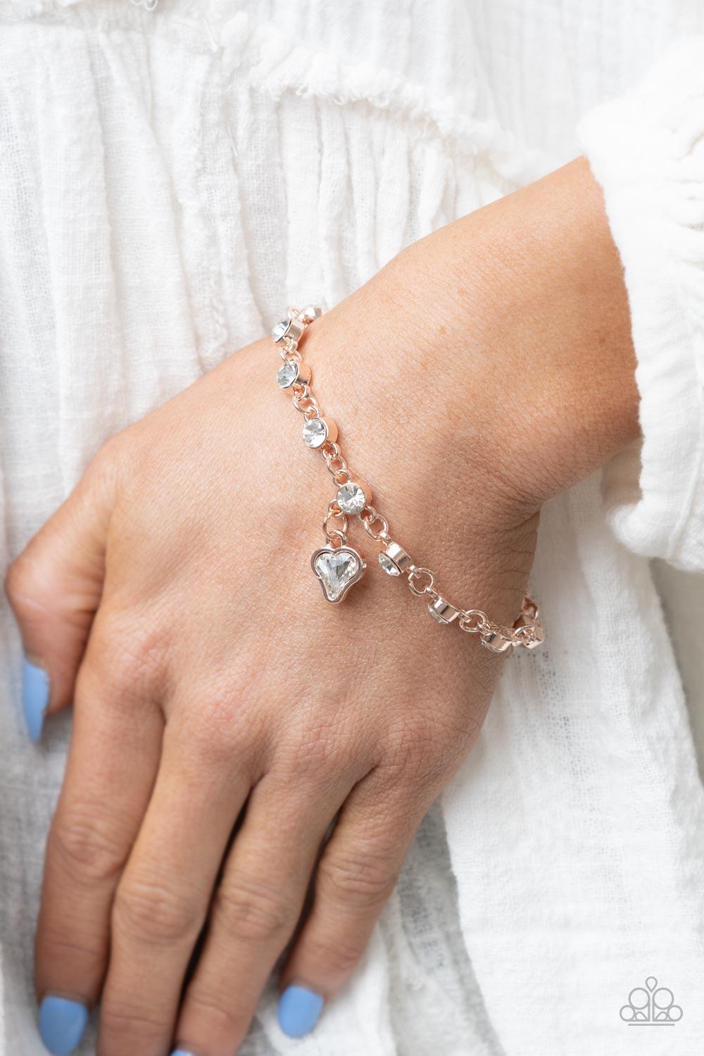 Paparazzi Accessories Sweet Sixteen - Rose Gold Brilliant white rhinestones in rose gold settings are linked together and accented with a charming white rhinestone heart that dangles sweetly from the wrist. Features an adjustable clasp closure. Sold as on