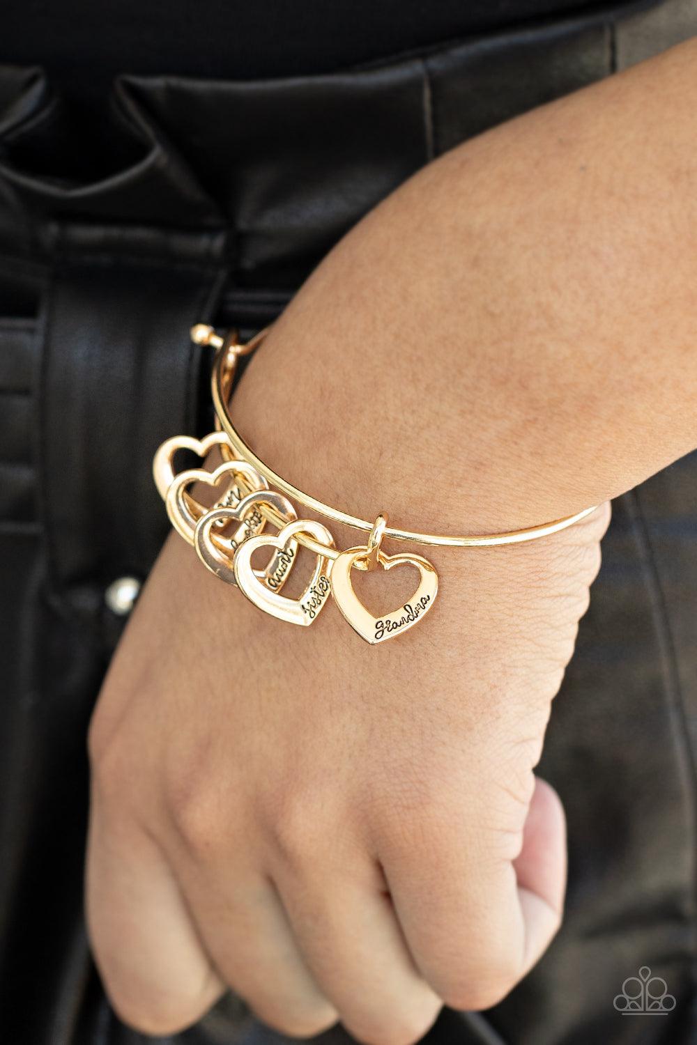 Paparazzi Accessories A Charmed Society - Gold A glistening collection of airy gold heart charms that are stamped in the words, "grandma," "sister," "aunt," "daughter," and "mom," glide along the center of a gold bangle-like bracelet. Features a pronged c