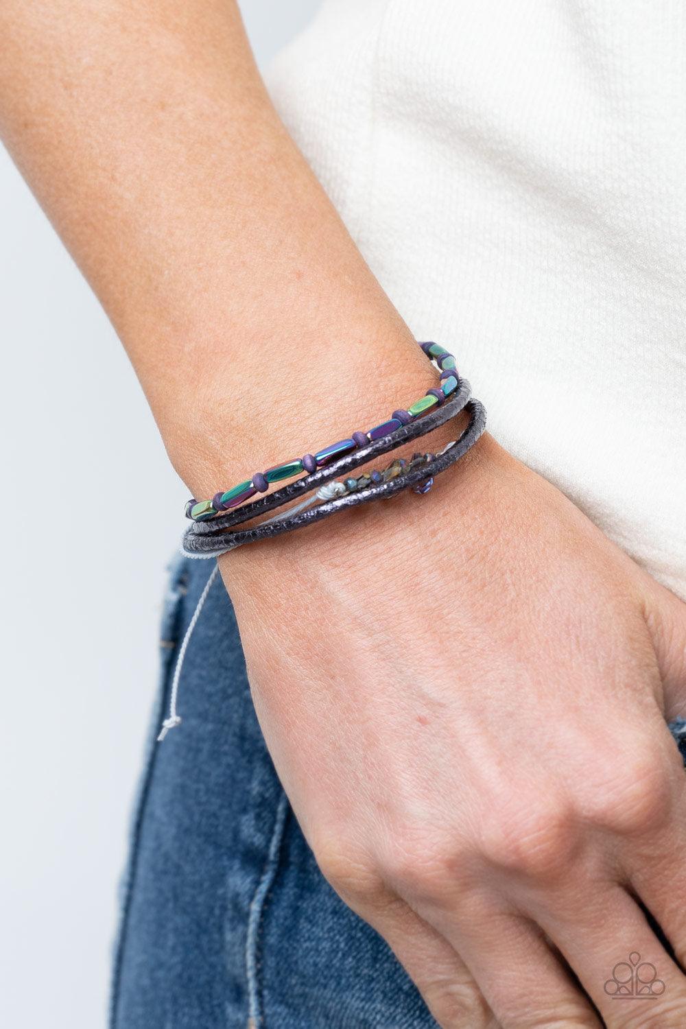 Paparazzi Accessories Holographic Hike - Multi A mismatched collection of oil spill beads, purple wooden beads, and iridescent crystal-like beads are threaded along gray threaded and glittery purple leather cording, creating stellar layers around the wris