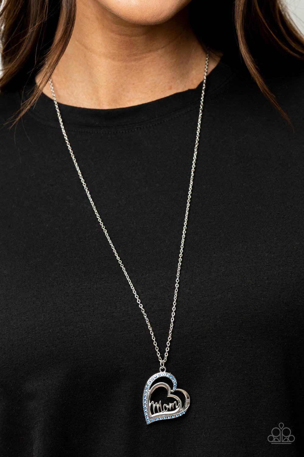 Paparazzi Accessories A Mothers Heart - Blue The word "Mom" floats inside an airy heart-shaped frame. A second heart encrusted with dewy blue rhinestones encircles the centerpiece as it sways from a lengthened silver chain for a sweet token of love. Featu