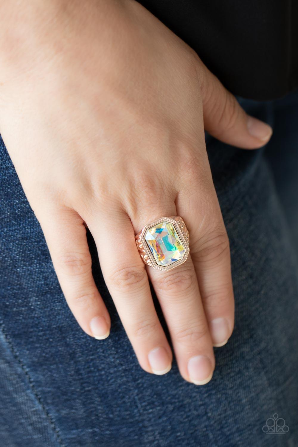 Paparazzi Accessories Galaxy Goddess - Rose Gold Featuring a dramatic UV shimmer, an oversized emerald cut gem is pressed into the center of a thick rose gold frame embossed in leafy patterns for a stellar statement atop the finger. Features a stretchy ba