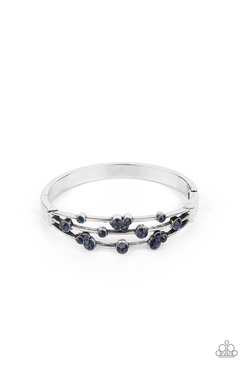 Paparazzi Accessories Cosmic Candescence - Blue A smattering of glittery blue rhinestones adorn three silver bars that coalesce into a versatile silver cuff-like bangle around the wrist. Features a hinged closure. Sold as one individual bracelet. Jewelry
