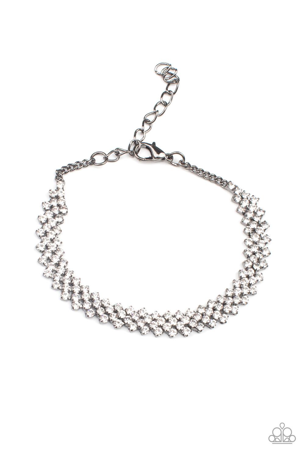 Paparazzi Accessories Chicly Candescent - Black Featuring sleek gunmetal fittings, dainty rows of glassy white rhinestones delicately slant across the wrist, coalescing into a timeless centerpiece. Features an adjustable clasp closure. Sold as one individ