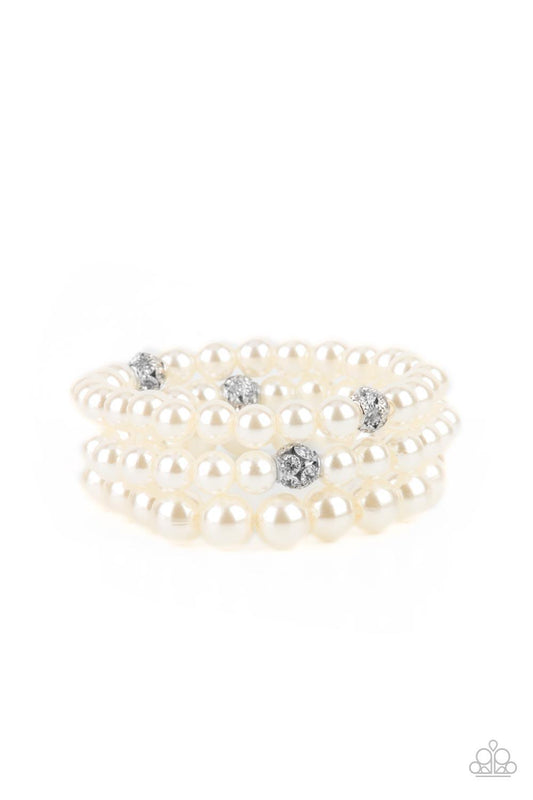 Paparazzi Accessories Here Comes The Heiress - White Infused with white rhinestone encrusted silver beads, a bubbly collection of mismatched white pearls are threaded along stretchy bands around the wrist for a vintage inspired layered look. Sold as one s