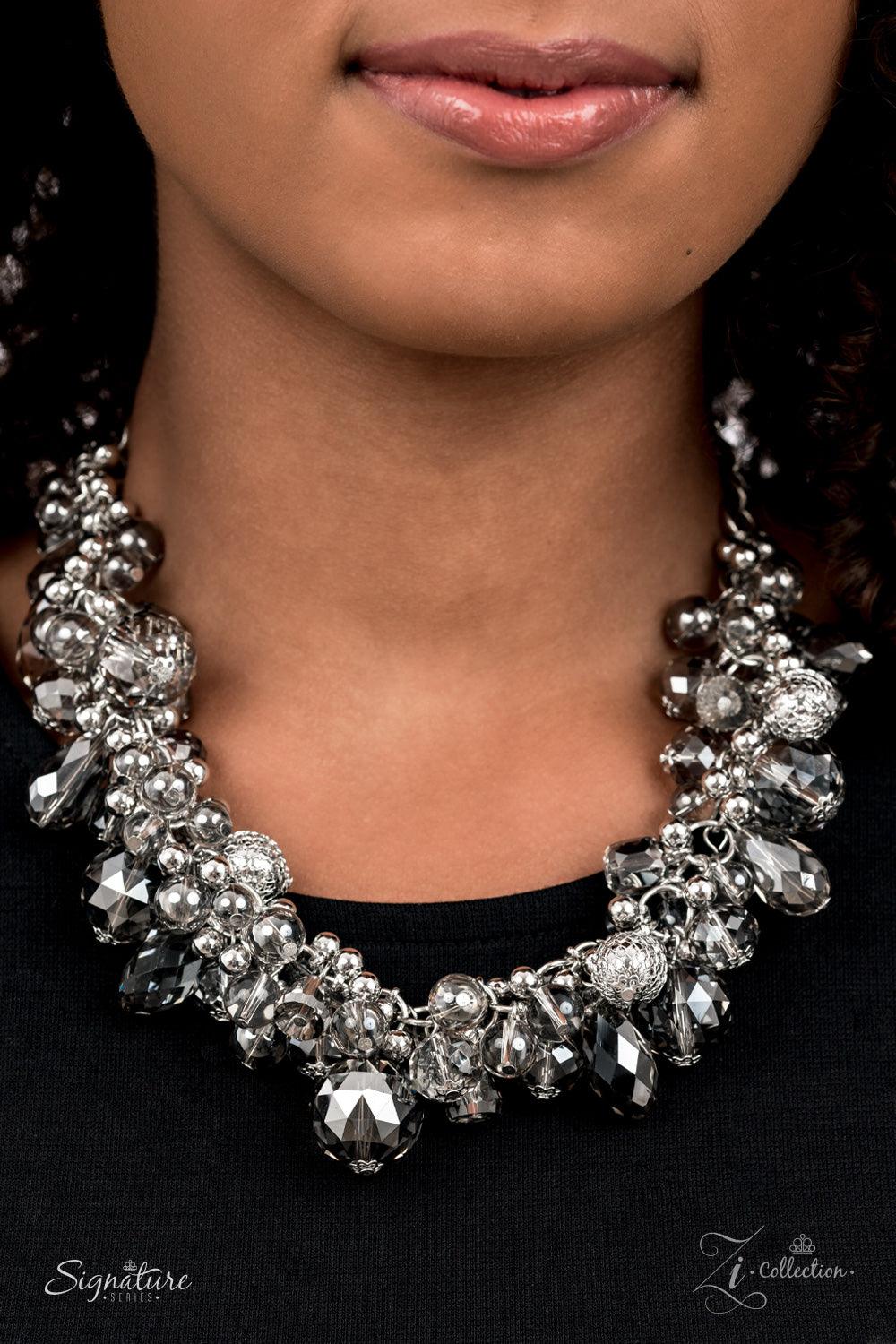 Paparazzi Accessories The Tommie Elegantly enhanced with classic silver and silvery wire mesh beads, a glassy glamorous collection of majestically mismatched smoky crystal-like beads capriciously cluster along a bold silver chain below the collar. Each fa