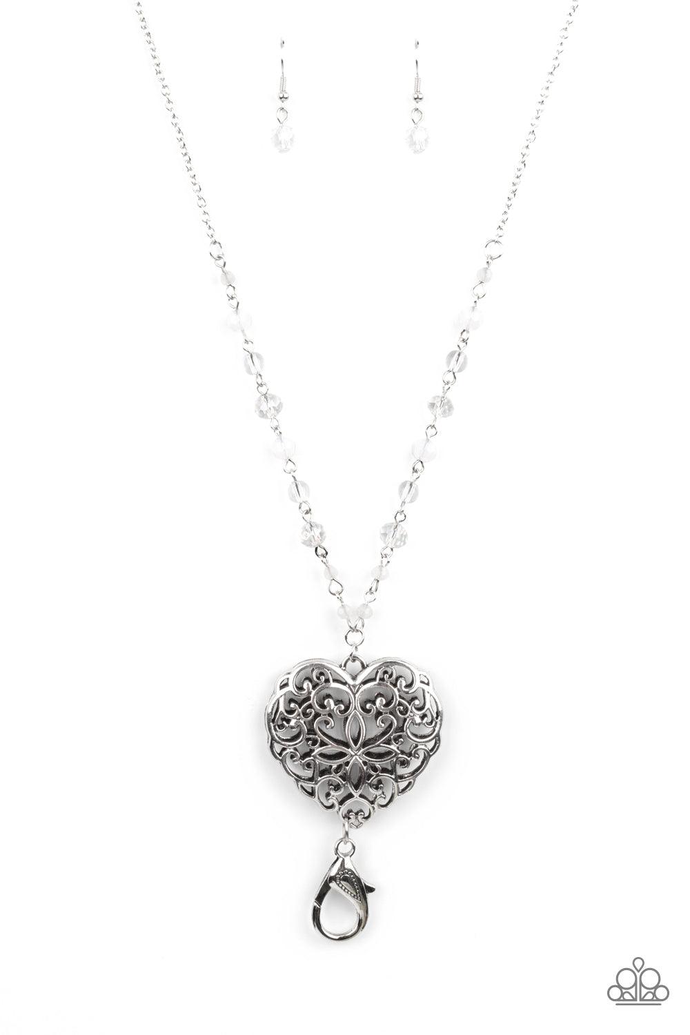Paparazzi Accessories Doting Devotion - White *Lanyard A dainty collection of opaque, glassy, and crystal-like beads give way to an oversized filigree filled heart frame, creating an antiqued locket inspired pendant at the bottom of a lengthened silver ch