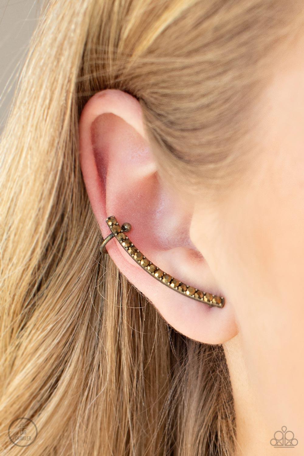Paparazzi Accessories Give Me The SWOOP - Brass Post Earring A dainty row of glitzy aurum rhinestones is encrusted along a gritty brass bar that swoops up the ear for a smoldering style. Features a dainty cuff attached to the top for a secure fit. Sold as