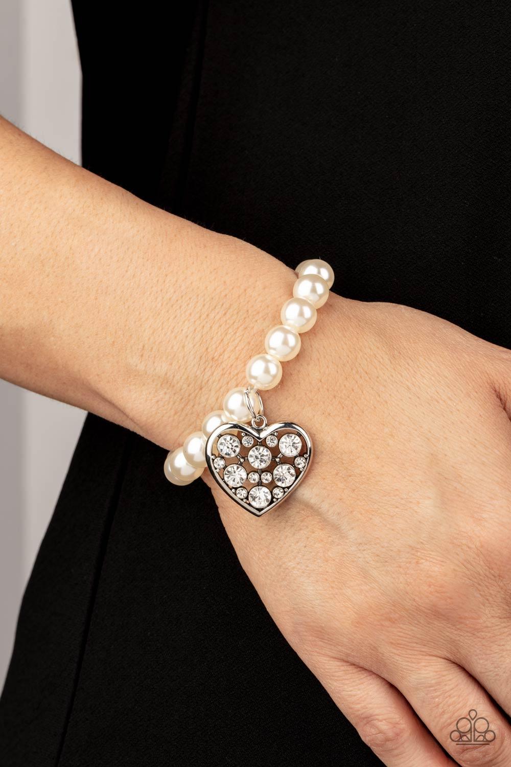 Paparazzi Accessories Cutely Crushing - White A dramatically oversized white rhinestone encrusted silver heart charm dangles from a stretchy strand of bubbly white pearls, creating a flirtatious dazzle. Sold as one individual bracelet. Jewelry