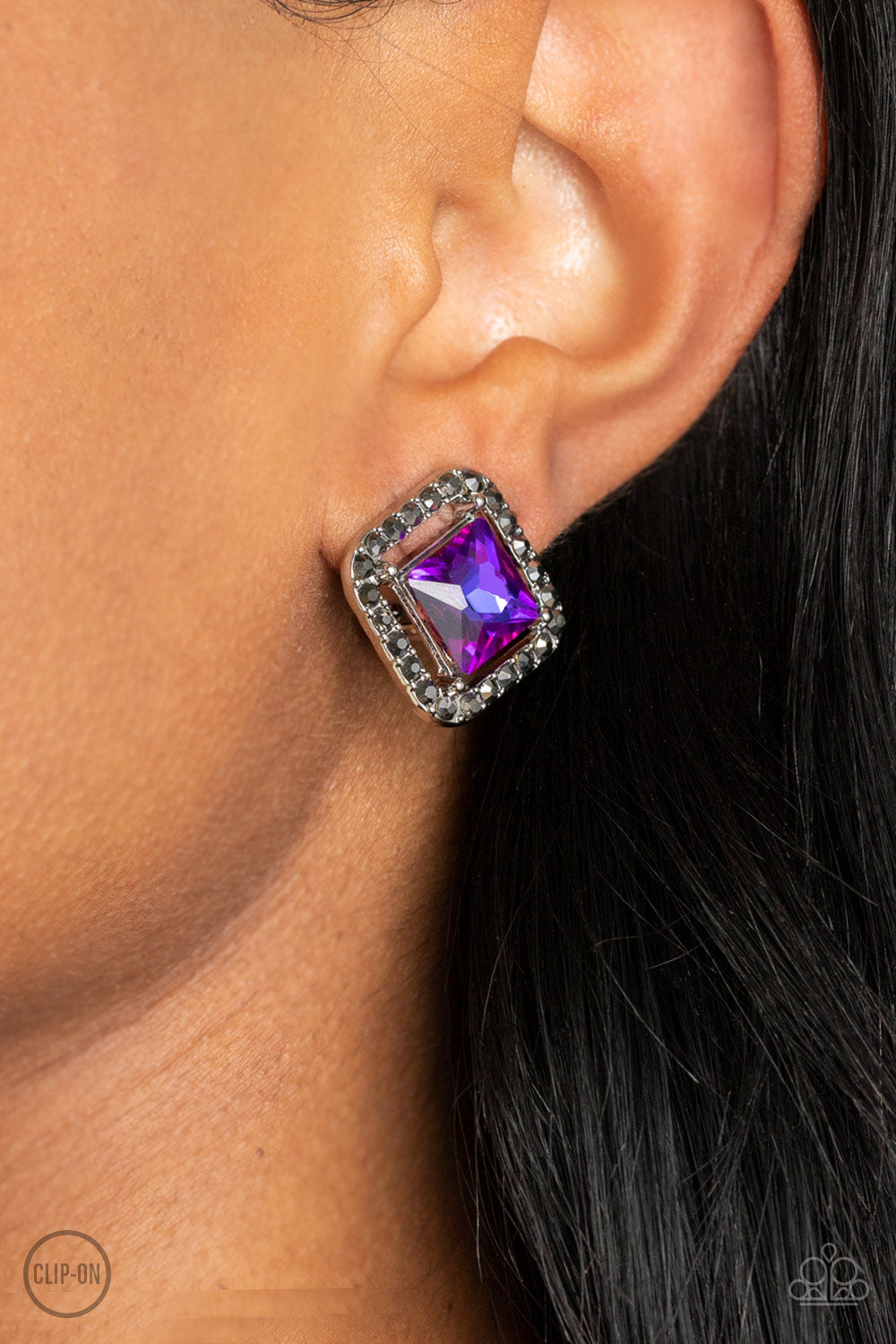 Paparazzi Accessories Cosmic Catwalk - Purple *Clip-On Featuring an iridescent UV finish, an emerald cut purple gem seemingly floats in the center of a hematite rhinestone encrusted frame for a stellar statement. Earring attaches to a standard clip-on fit