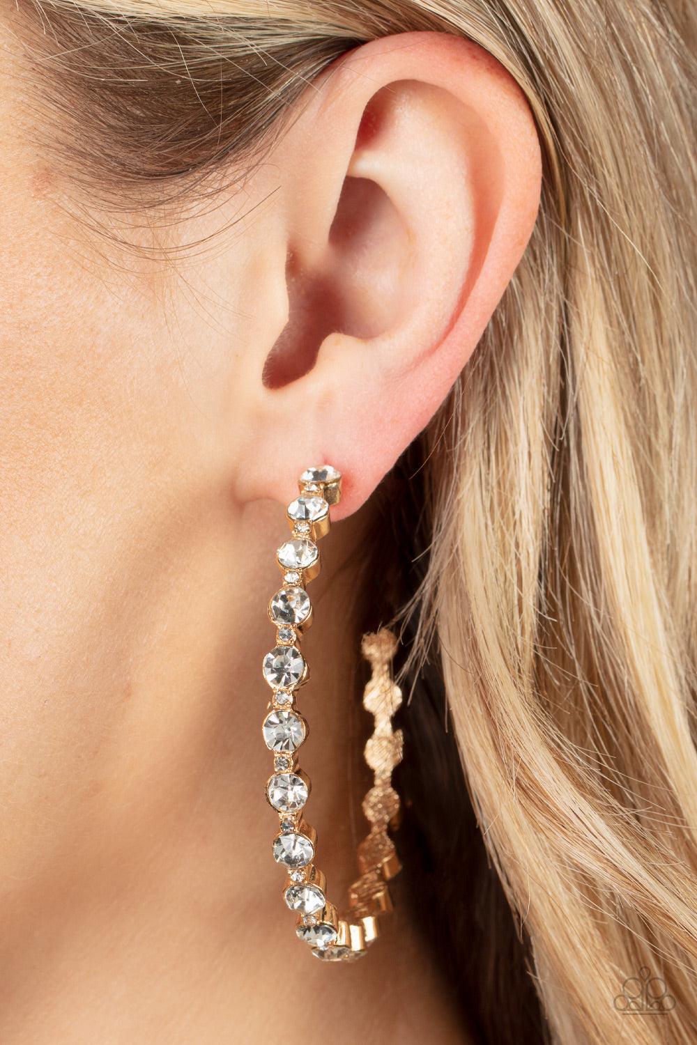 Paparazzi Accessories Royal Reveler - Gold Encased in sleek gold fittings, a glamorous collection of glittery white rhinestones delicately coalesce into an oversized hoop for a sparkly statement. Earring attaches to a standard post fitting. Hoop measures