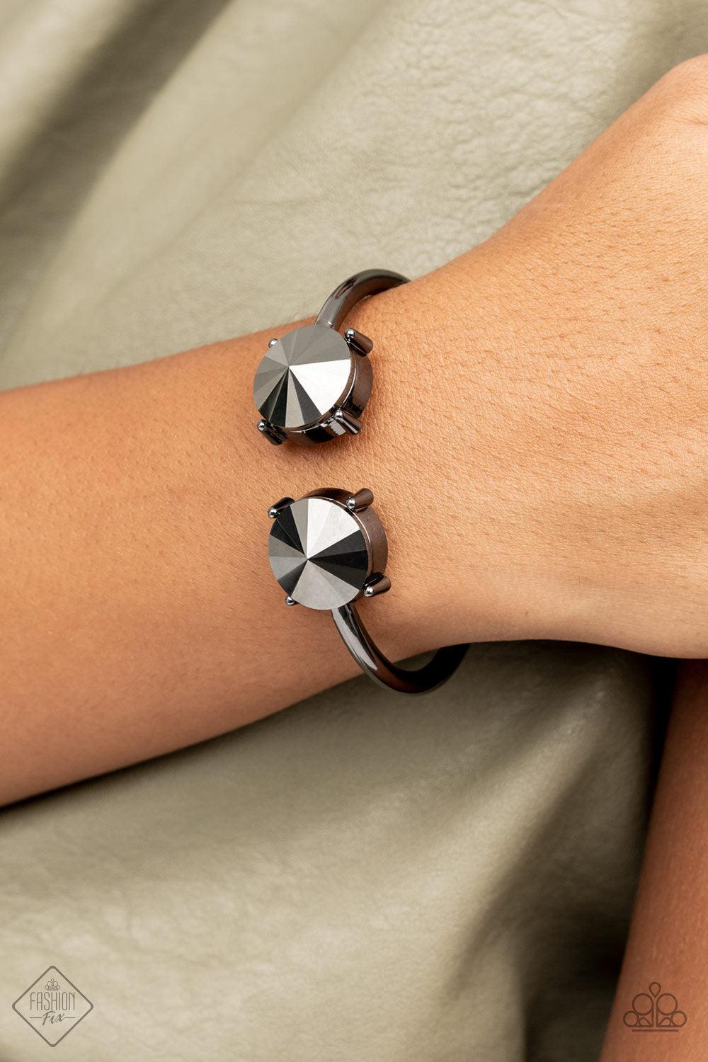 Paparazzi Accessories Spark and Sizzle - Black Two dramatically oversized hematite rhinestones are nestled inside pronged gunmetal fittings at the ends of a hinged gunmetal cuff, creating a smoldering statement piece that wraps boldly around the wrist. Fe
