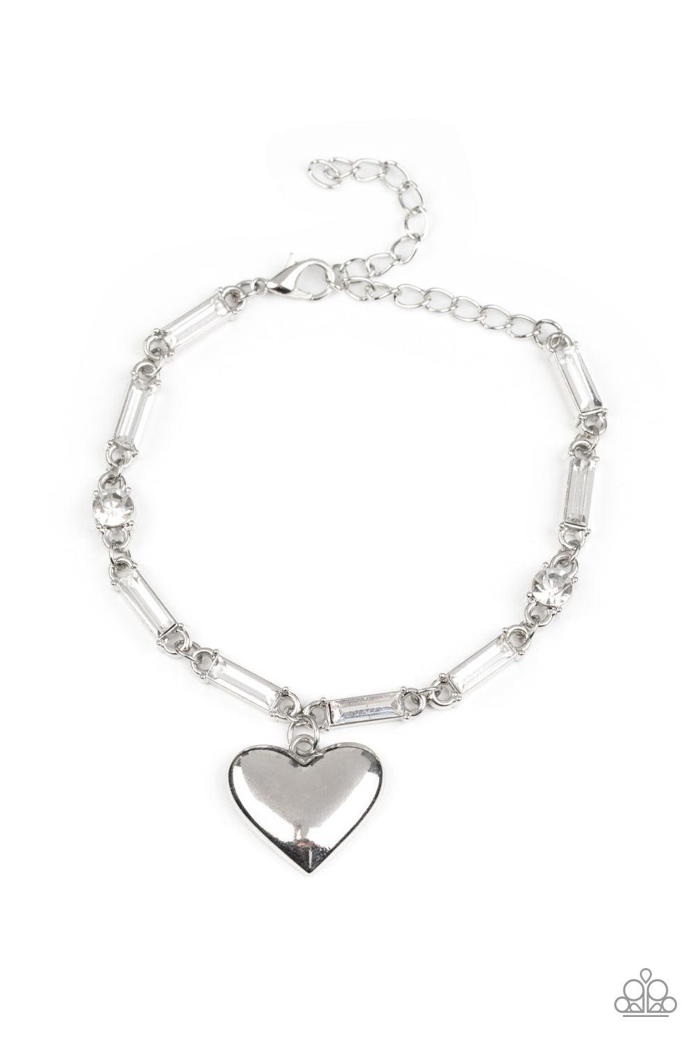 Paparazzi Accessories Sweetheart Secrets - White Encased in sleek silver fittings, round and emerald cut rhinestones delicately link into a sparkly chain around the wrist. A shiny silver heart charm swings from the glittery compilation, adding a flirtatio