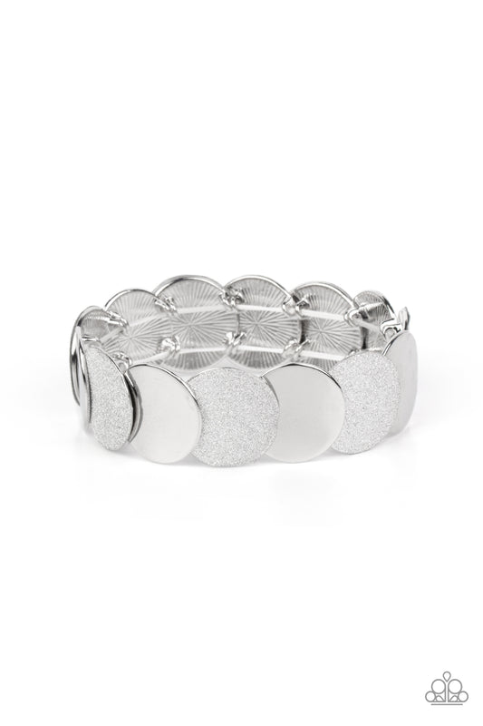 Paparazzi Accessories Demurely Disco - Silver A glimmering collection of shiny silver discs and glitter coated silver discs delicately overlap along stretchy bands around the wrist, creating a dazzling hint of shimmer. Sold as one individual bracelet. Bra