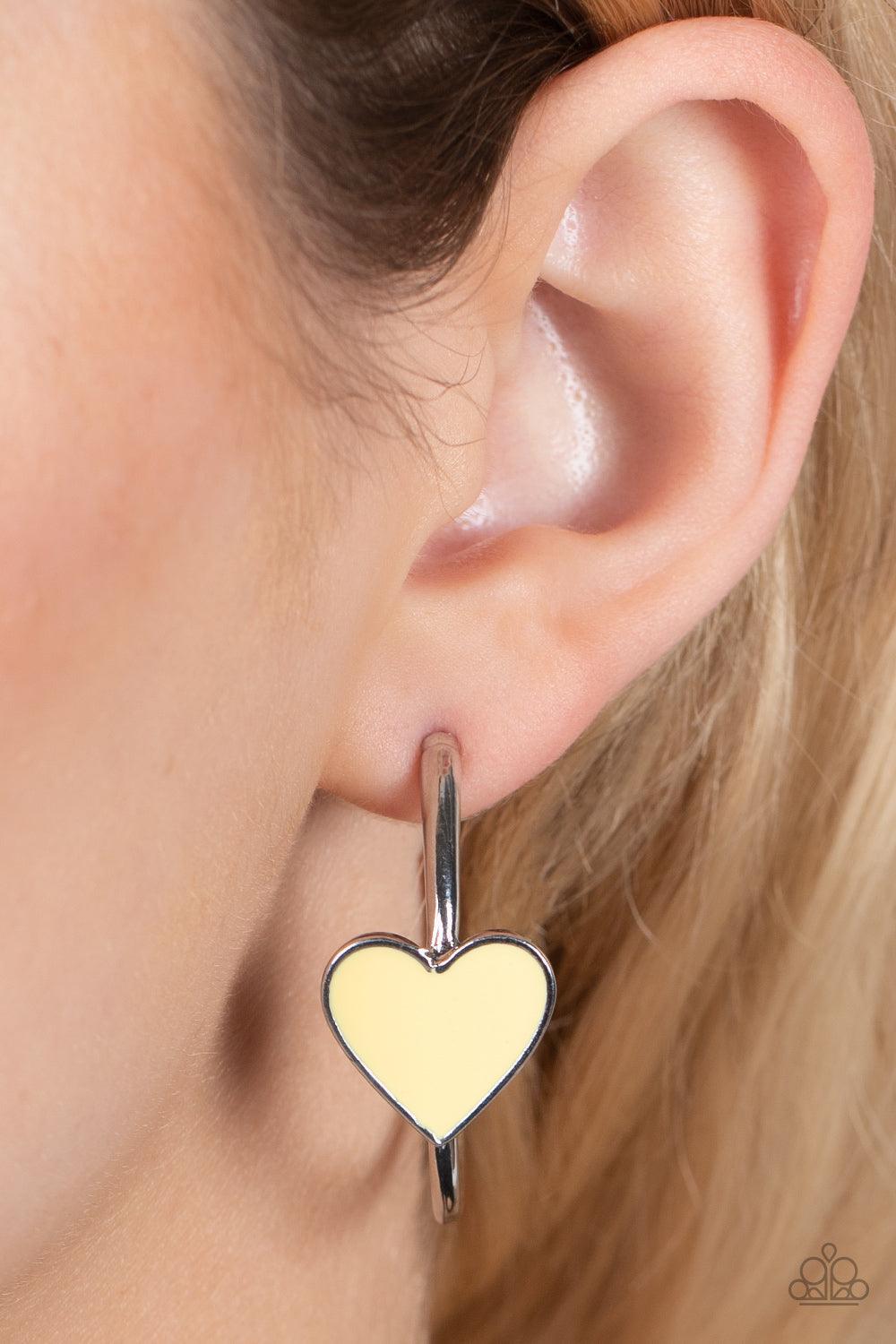 Paparazzi Accessories Kiss Up - Yellow A charming Illuminating heart adorns the front of a classic silver hoop resulting in a whimsical fashion. Earring attaches to a standard post fitting. Hoop measures approximately 1 1/4" in diameter. Sold as one pair