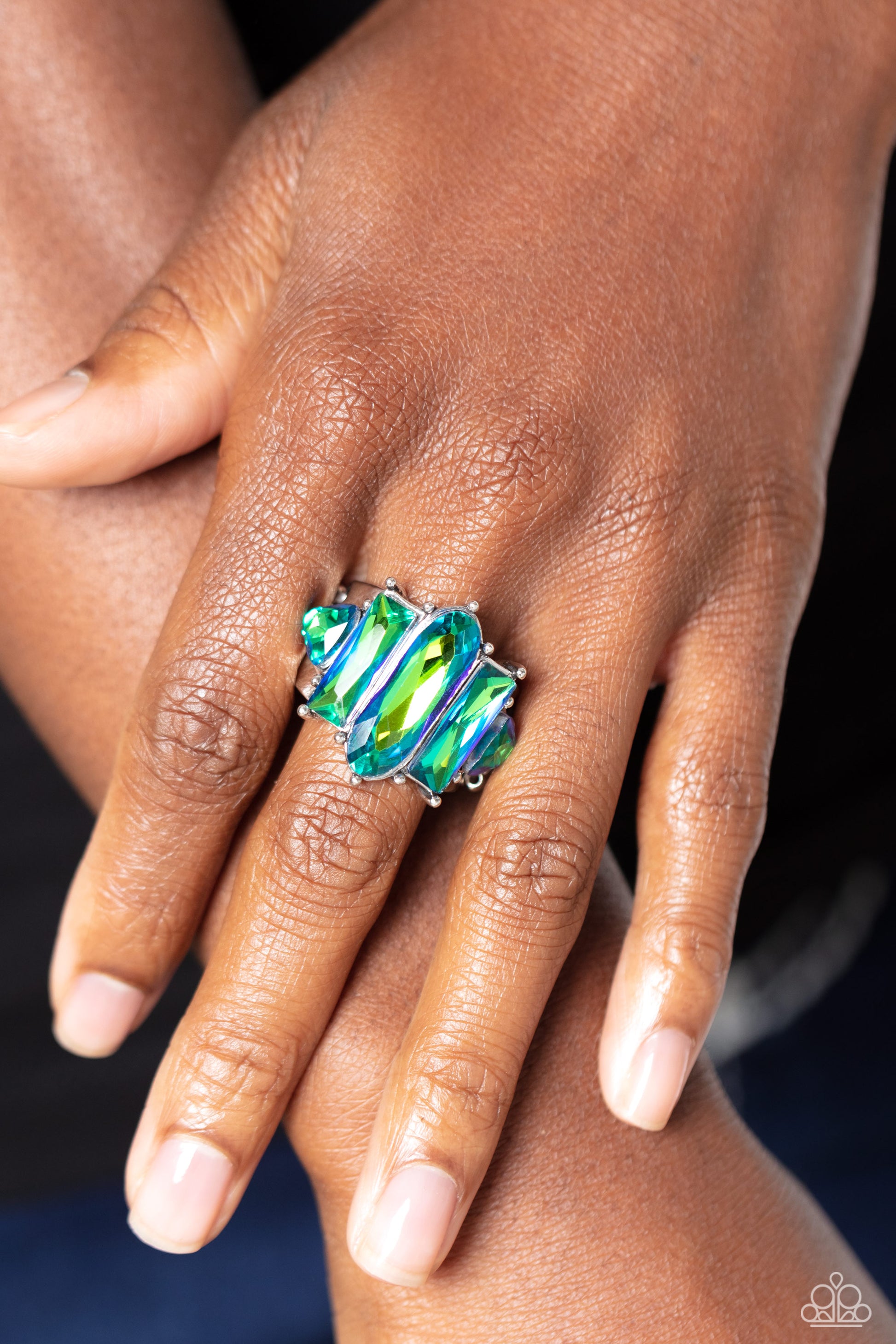 Paparazzi Accessories Iridescently Interstellar - Green Featuring a stellar UV finish, an iridescent collection of triangular, emerald, and oval cut green rhinestones are encrusted across the center of a thick silver band for an out-of-this-world fashion.