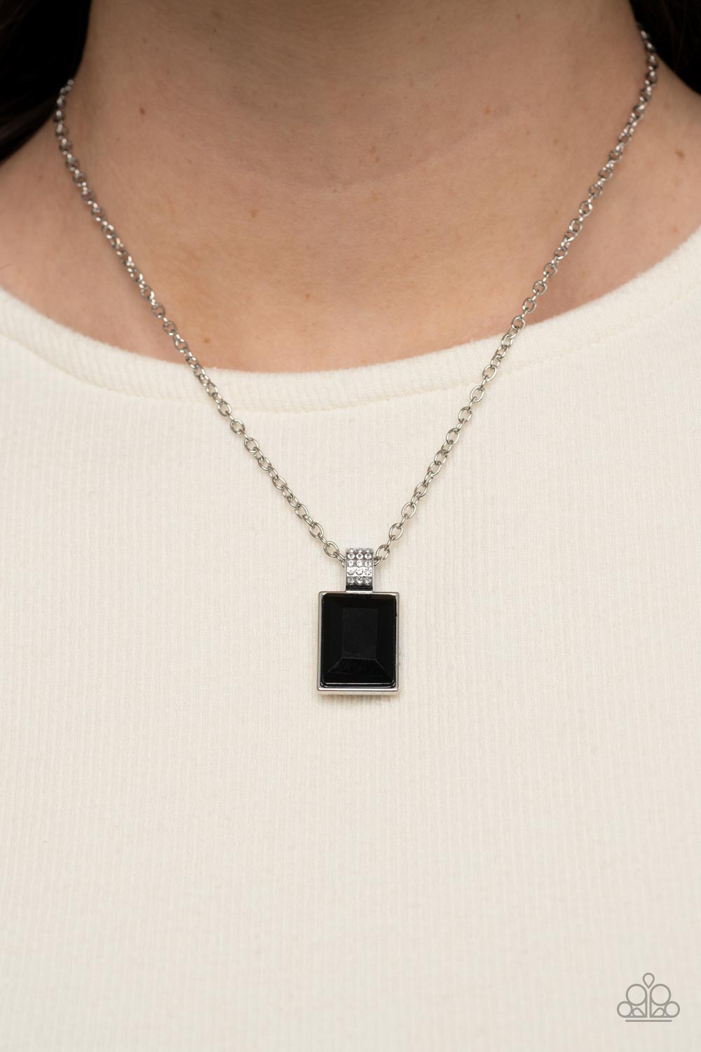 Paparazzi Accessories Understated Dazzle - Black Featuring a white rhinestone encrusted silver fitting, an oversized emerald cut black rhinestone swings from the bottom of a dainty silver chain below the collar for a glamorous fashion. Features an adjusta