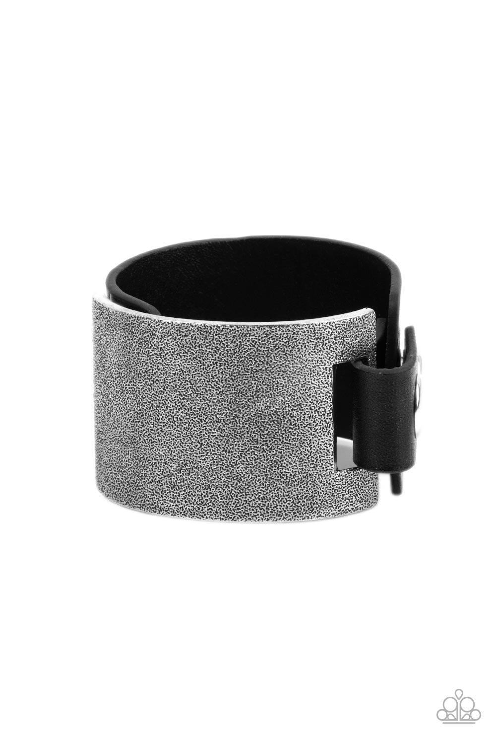 Paparazzi Accessories Studded Synchronism - Black A curved tin finished silver panel, coated in antiqued texture, attaches to a wide black leather band with silver snaps resulting in an edgy industrial element around the wrist. Features an adjustable snap