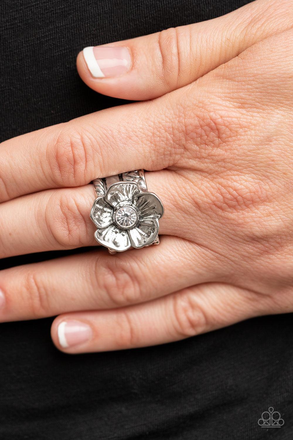 Paparazzi Accessories Prismatically Petunia - White Textured silver petals gently gather around a sparkling white rhinestone center, blooming into a dazzling floral centerpiece atop the finger. Features a stretchy band for a flexible fit. Sold as one indi