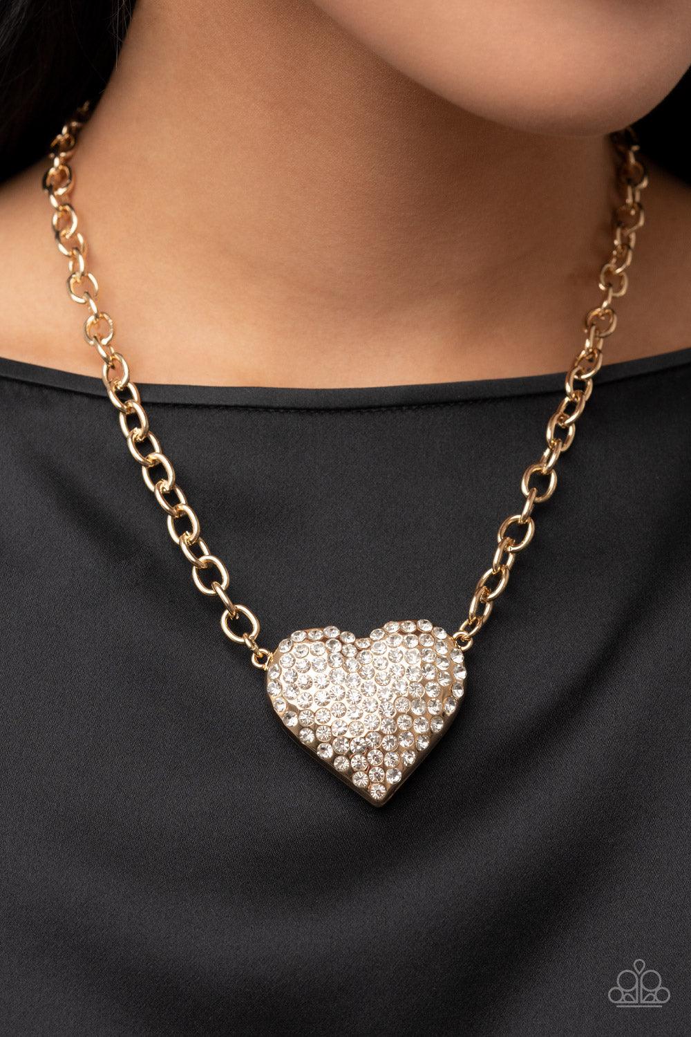 Paparazzi Accessories Heartbreakingly Blingy - Gold A dramatically oversized gold heart frame is encrusted in row after row of dazzling white rhinestones, resulting in a heart-racing sparkle below the collar. Features an adjustable clasp closure. Sold as