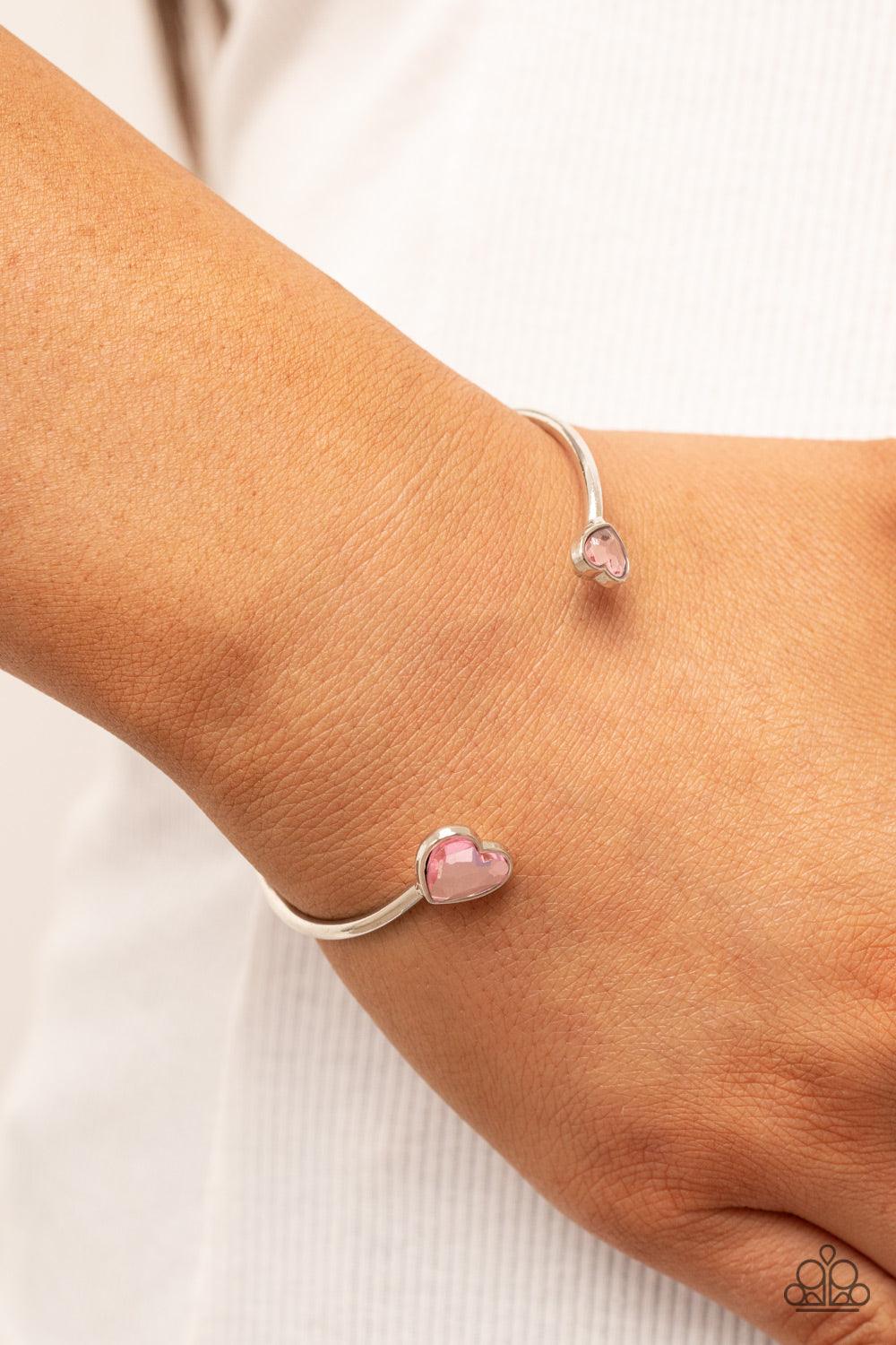 Paparazzi Accessories Unrequited Love - Pink Enhanced with glitzy pink rhinestones, two silver hearts adorn the ends of a silver band that curls around the wrist for a flirtatious open-faced style cuff. Sold as one individual bracelet. Bracelets