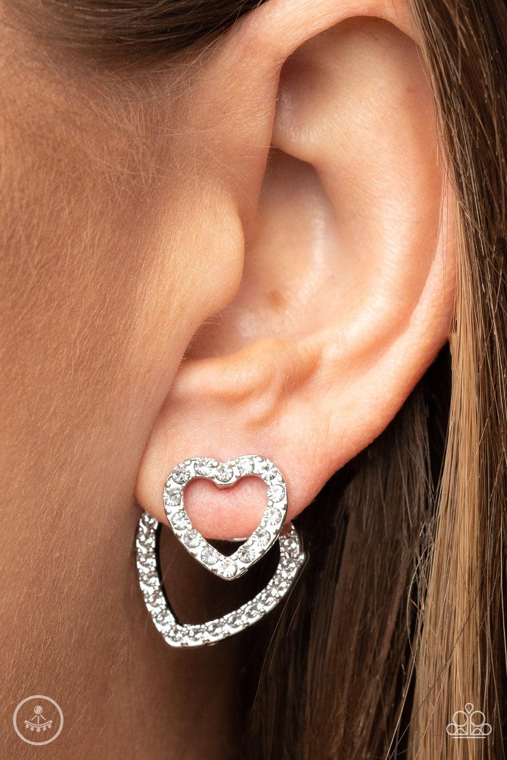 Paparazzi Accessories Ever Enamored - White A dainty silver heart dotted in glassy white rhinestones flirtatiously attaches to a double-sided post, while a slightly larger white rhinestone encrusted silver heart peeks out beneath the ear for a romantic fi