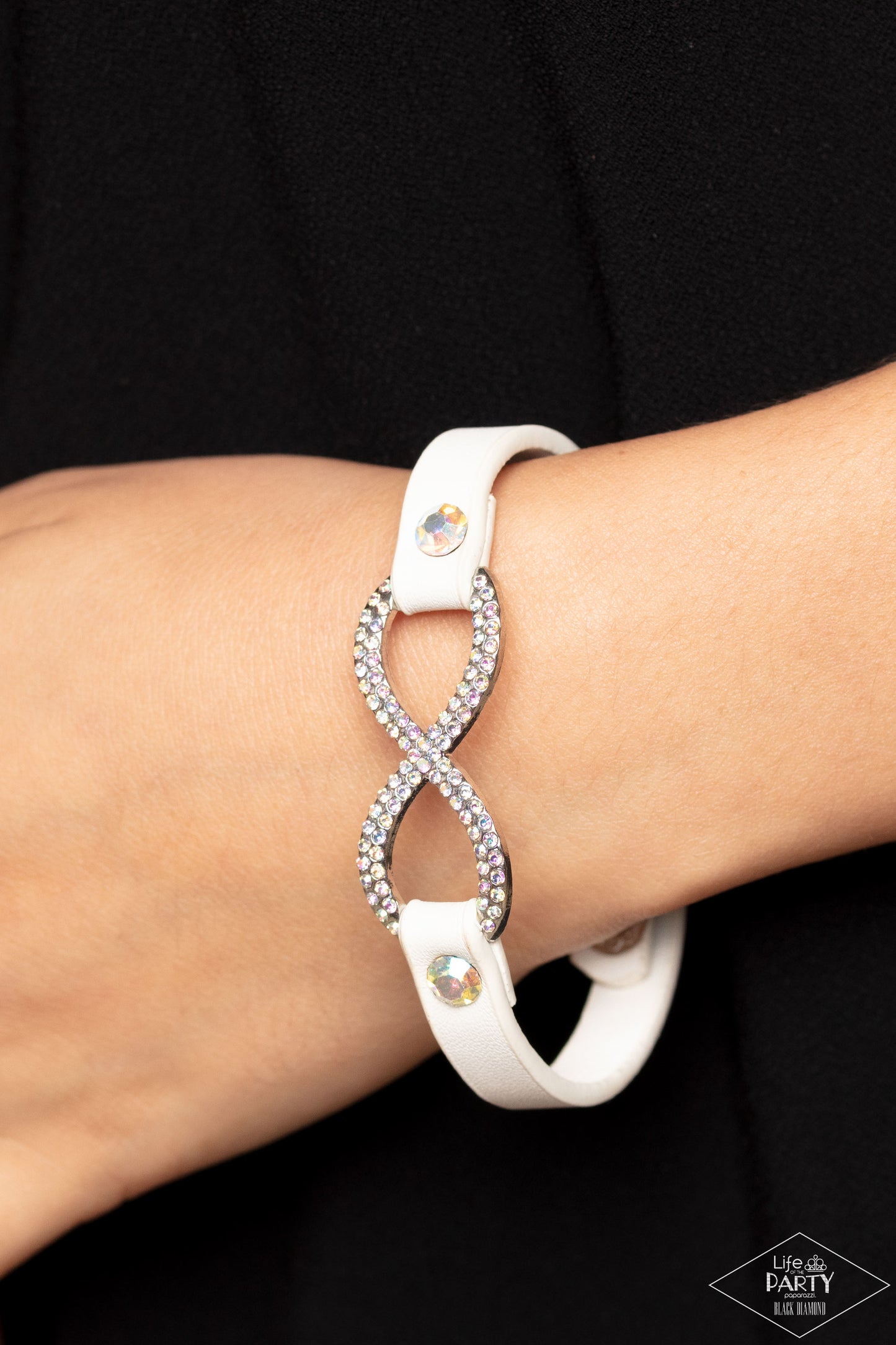 Paparazzi Accessories Innocent Till Proven GLITZY! - Multi A skinny strip of white leather attaches to a silver infinity symbol encrusted in glittery iridescent rhinestones. Flanked by two dazzling solitaire iridescent rhinestones, the glitzy design creat