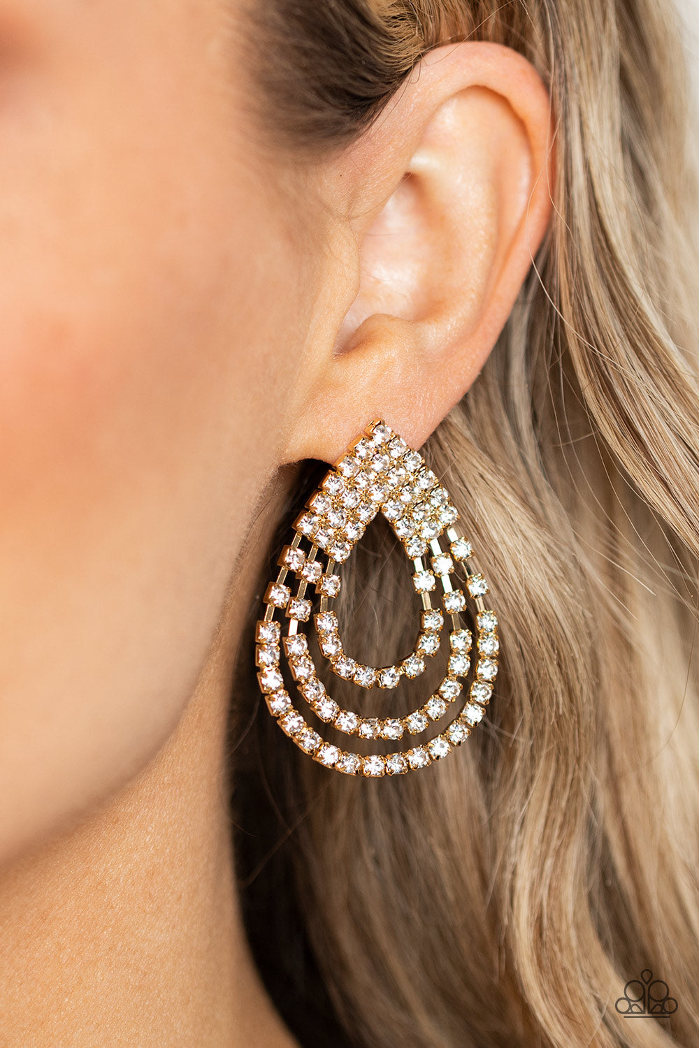 Paparazzi Accessories Take a POWER Stance - Gold Loops of glassy white rhinestones ripple out from the bottom of a stationary triangular fitting that is dotted in glittery white rhinestones, resulting in a timeless teardrop chandelier. Earring attaches to