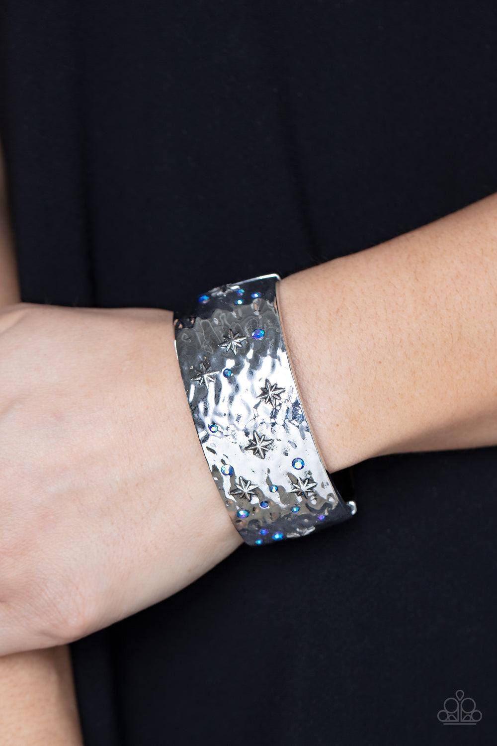 Paparazzi Accessories Across the Constellations - Blue Twinkling with dainty silver stars, hammered silver frames are adorned with a smattering of iridescent blue rhinestones as they delicately join into a bangle-like bracelet around the wrist. Due to its