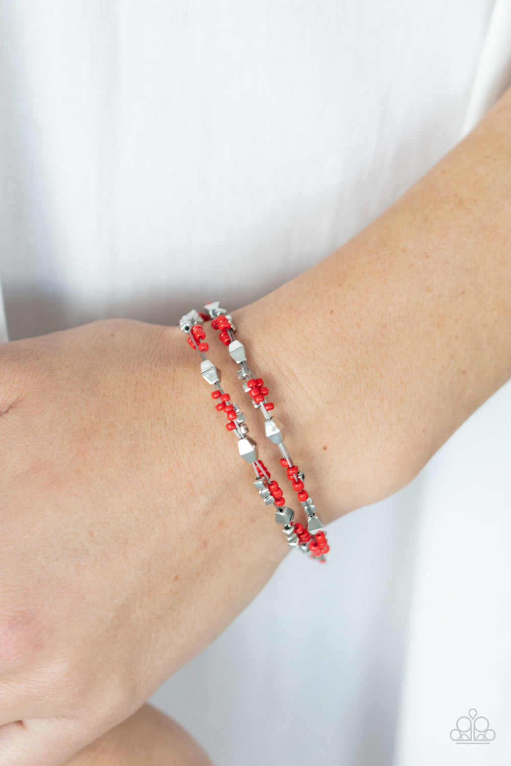 Paparazzi Accessories Elite Explorer - Red A dainty collection of faceted silver beads, red seed beads, and silver cubes are threaded along multiple strands of silver wire around the wrist, creating clustered layers. Features an adjustable clasp closure.