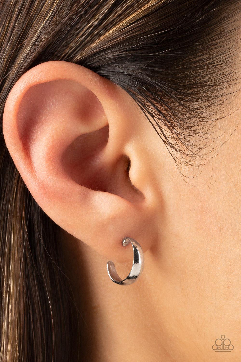 Paparazzi Accessories Mini Magic - Silver Featuring a high-sheen, a slightly flared smooth silver bar curves into a dainty hoop resulting in a basic staple piece perfect for layering. Earring attaches to a standard post fitting. Hoop measures approximatel
