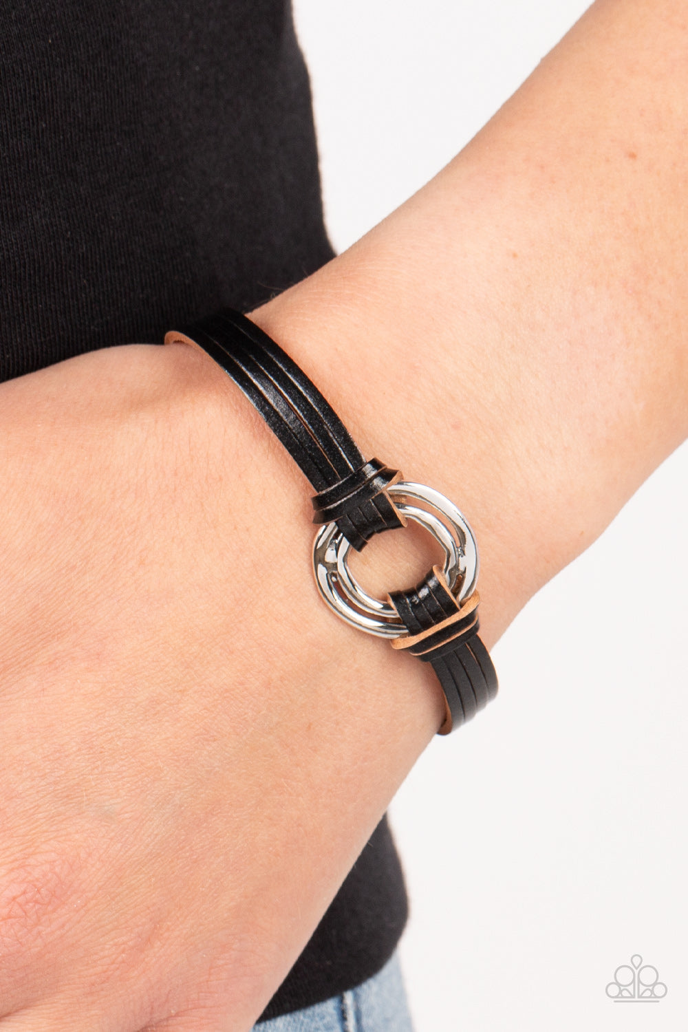 Paparazzi Accessories Free Range Fashion - Black Black leather strips knot around a soldered pair of asymmetrical hoops, knotting the rustic frame in place at the center of the wrist for a free-spirited finish. Features a magnetic closure. Sold as one ind