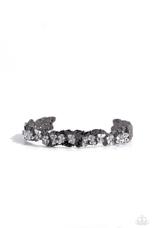 Paparazzi Accessories Enticingly Icy - Black Featuring raw cuts, pairs of icy white gems are fitted in place across the center of a hammered and asymmetrical gunmetal cuff with dainty gunmetal wires. Reminiscent of ice, the sharp rhinestone accents are ha