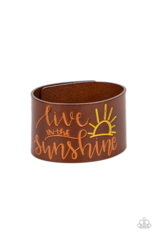 Paparazzi Accessories Sunshine Season - Orange A thick band of light brown leather is stamped with the cheerful phrase, "live in the sunshine," along with a radiating sun design. The orange font complements the yellow tint of the sun in an optimistic fini