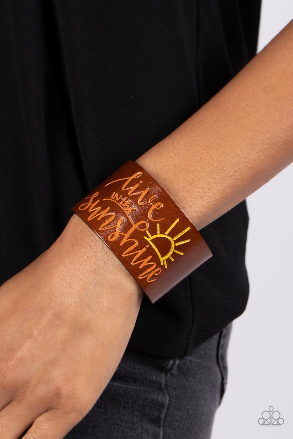 Paparazzi Accessories Sunshine Season - Orange A thick band of light brown leather is stamped with the cheerful phrase, "live in the sunshine," along with a radiating sun design. The orange font complements the yellow tint of the sun in an optimistic fini
