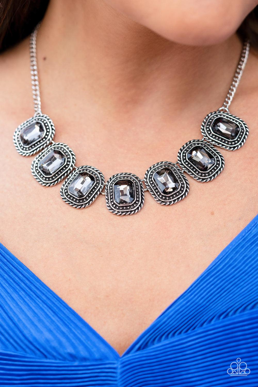 Paparazzi Accessories Iced Iron - Silver Pressed into silver, chain-like frames, radiant-cut hematite rhinestones smolder below the collar in a jaw-dropping finish. Each frame is embellished with twisted texture and subtle silver studs, bringing a gritty